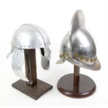 Two metal helmets on stands, one in design of a Spanish Conquistador, the other of Roman solider
