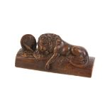 Wooden sculpture in the form of a lion lying on shields and spears. Length: 14.5cm.