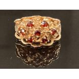 A 9CT YELLOW GOLD SEVEN STONE GARNET RING SET IN AN ORNATE SETTING SIZE K 1/2 4.8G GROSS