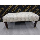 A LARGE UPHOLSTERED FOOTSTOOL ON BRASS CASTORS 93CM BY 49CM BY 40CM