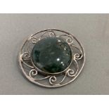 SILVER ORNATE BROOCH SET WITH LARGE GREEN/YELLOW ROUND SHAPED STONE IN THE CENTRE WITH SCROLL EDGING