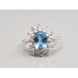 9CT YELLOW GOLD BLUE TOPAZ AND DIAMOND CLUSTER RING FEATURING AN OVAL SHAPED BLUE TOPAZ STONE IN THE