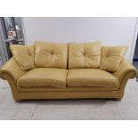 A mustard leather effect three piece suite comprising three seater, two seater and armchair.