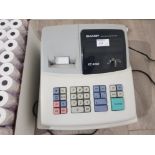 A Sharp electronic cash register XE-A102 together with a large quantity of receipt rolls.