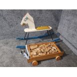 A painted wooden and metal rocking horse together with a wooden trolley full of building blocks.