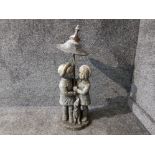 A composite stone garden ornament of children and a dog with metal umbrella by Henri Studio Inc
