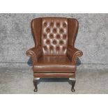 Brown leather metal studded wing back armchair, button back with mahogany feet