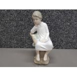 A Lladro figure of a boy sitting on a tree stump.