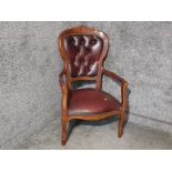 A carved wooden open armchair with red leatherette seat and buttoned back.