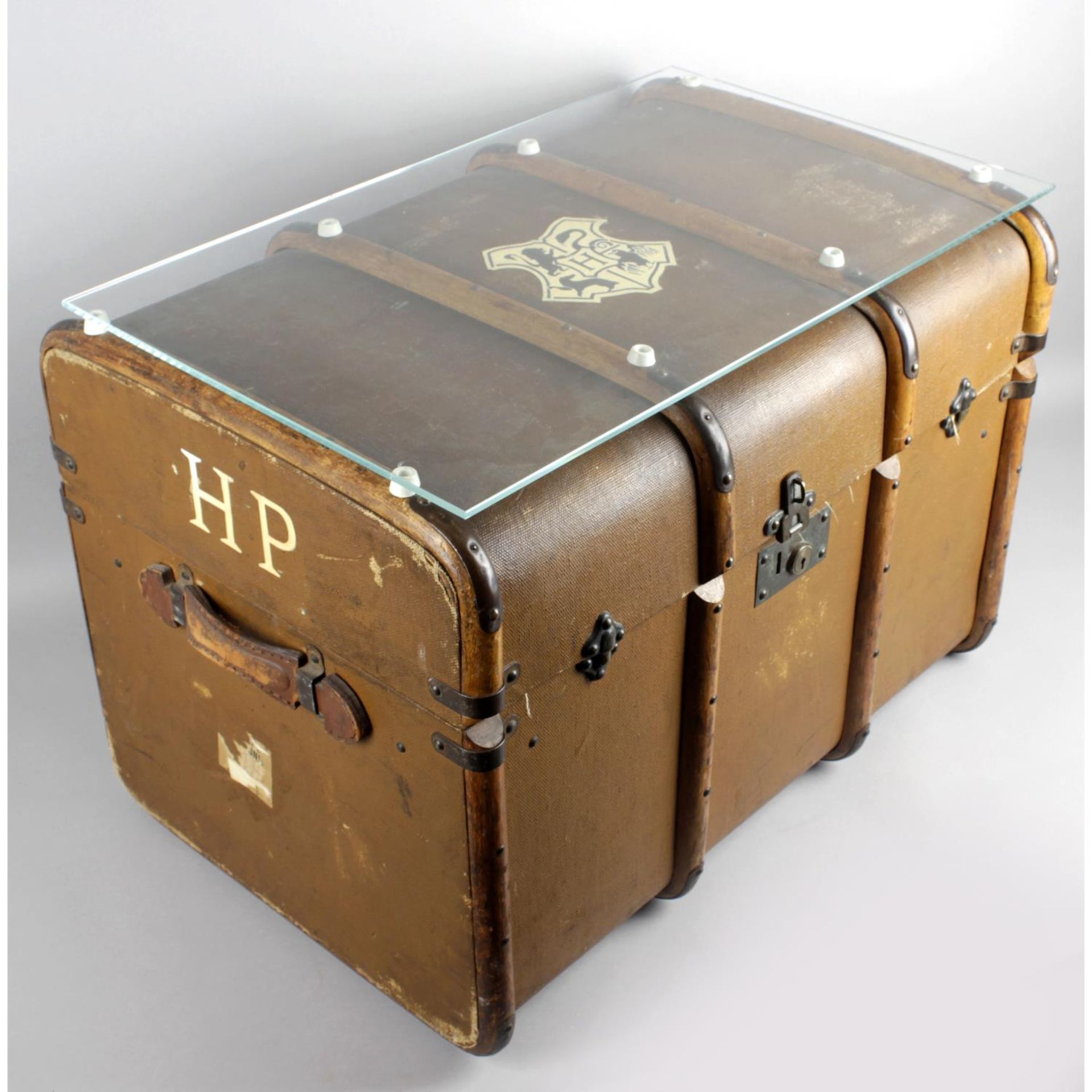 An old brown canvas and wooden bound travel trunk with applied Hogwarts crest to top and H.P