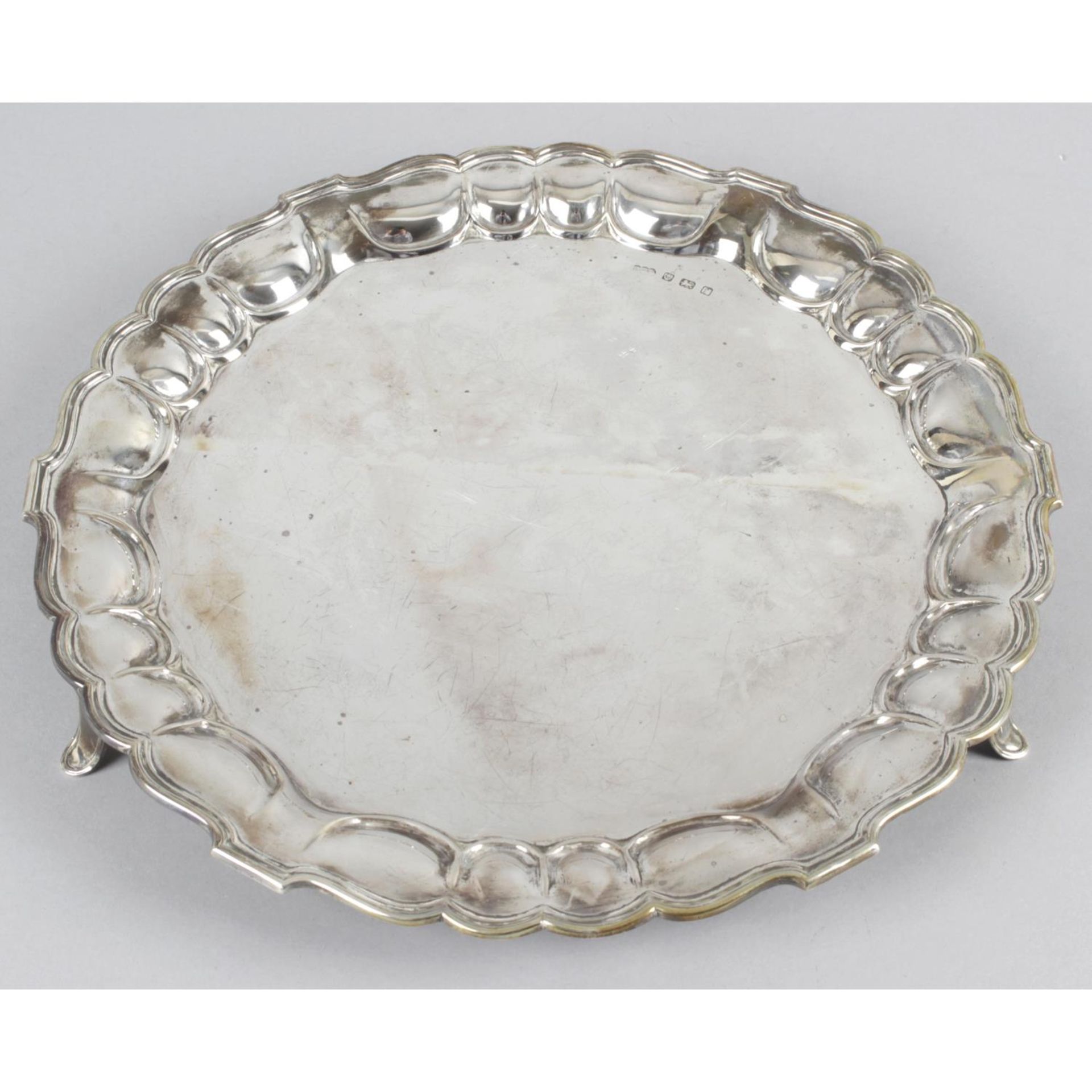 An Edwardian silver circular salver with scalloped edge and standing on three outward splaying
