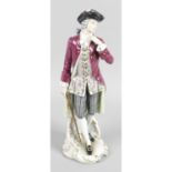 A continental porcelain figure modelled as a dandy standing dressed in a cocked hat and long coat,