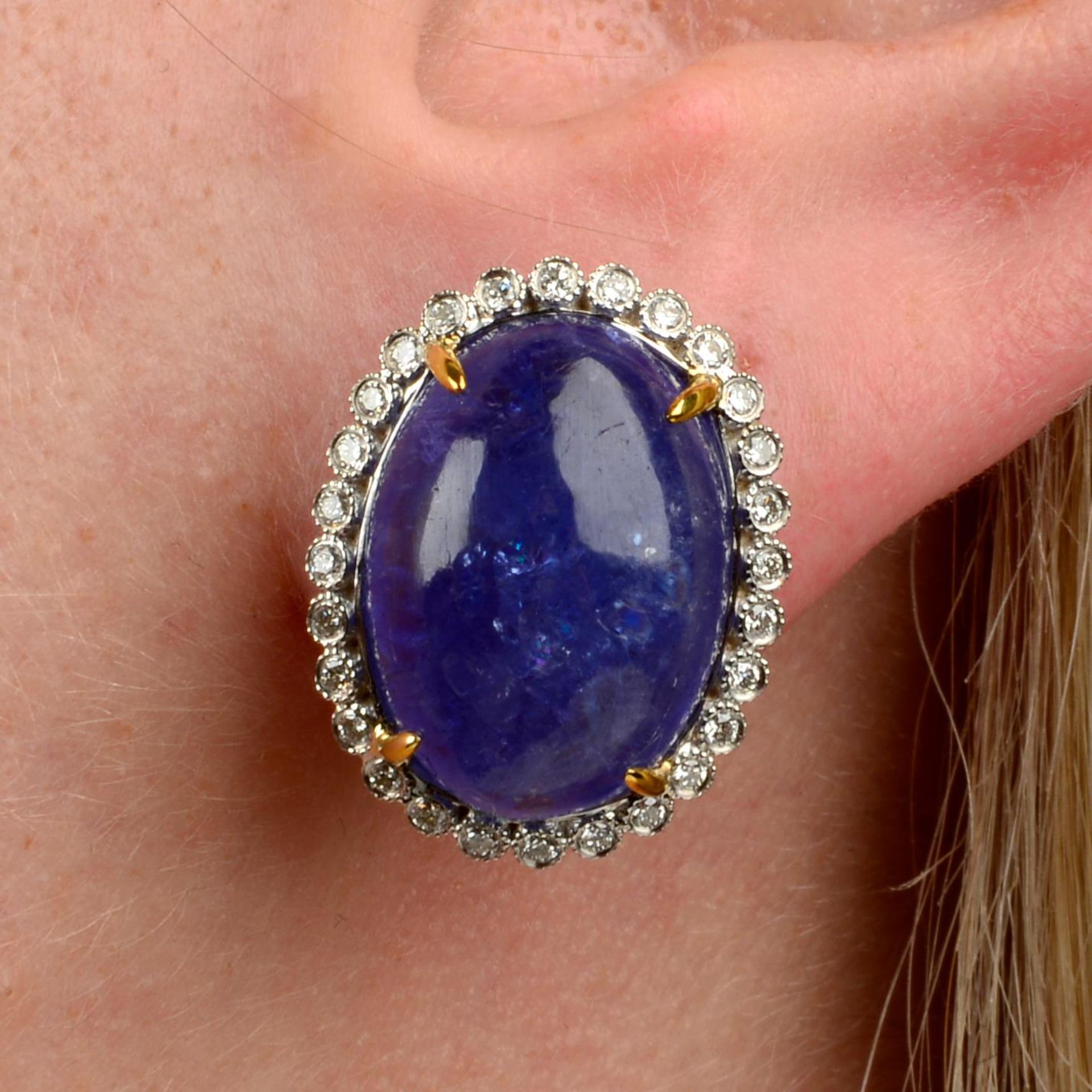 A pair of tanzanite cabochon and brilliant-cut diamond earrings.Total tanzanite weight