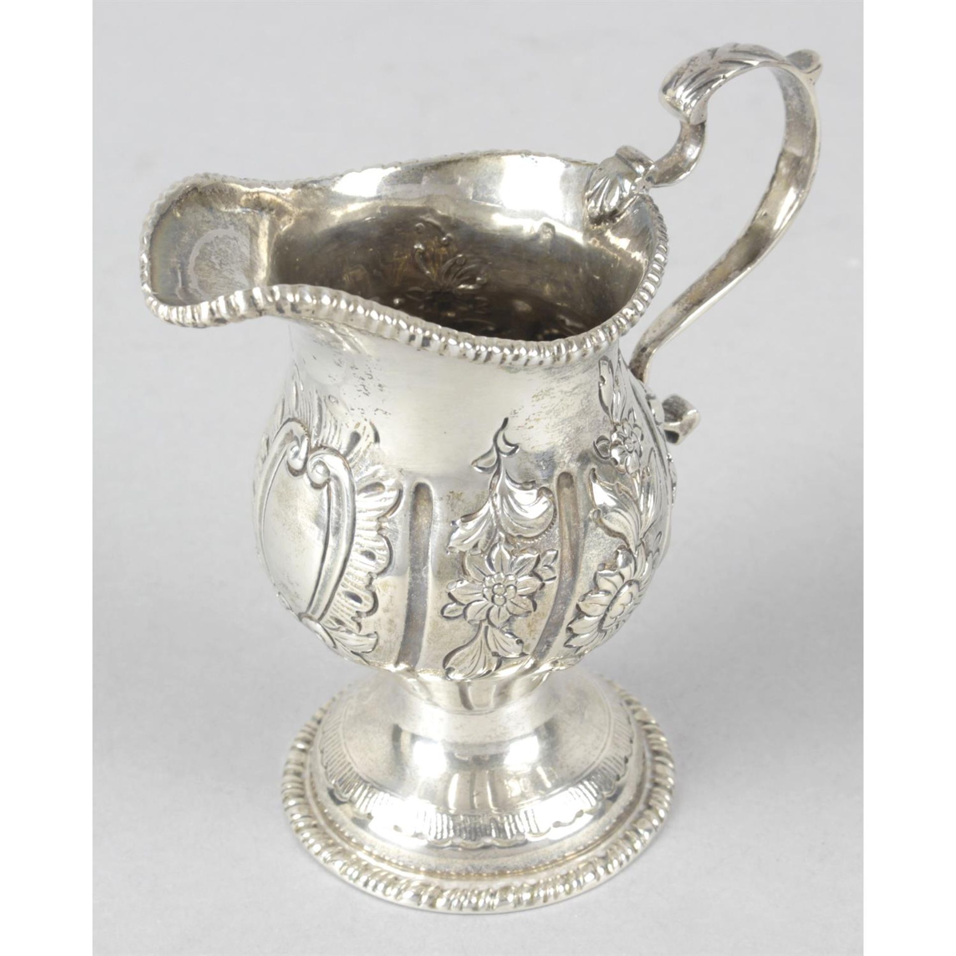 An Edwardian silver floral embossed pedestal cream jug.