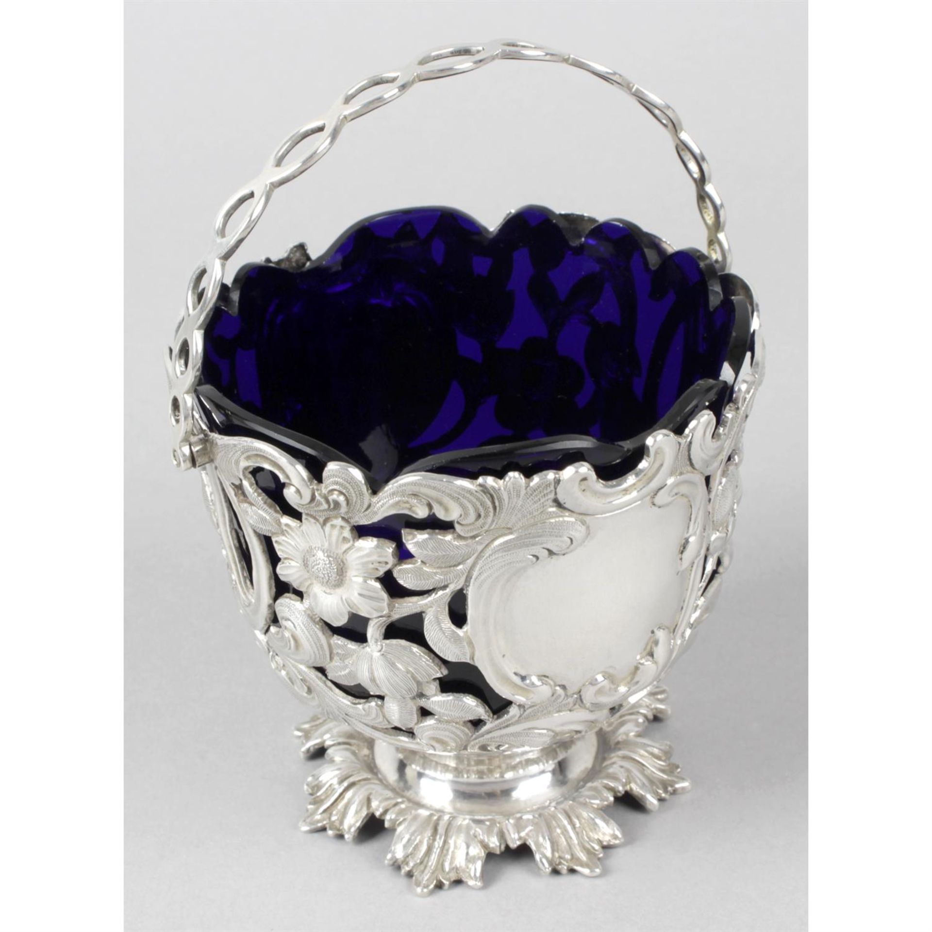 An early Victorian silver pierced and swing-handled sugar basket with blue glass liner.