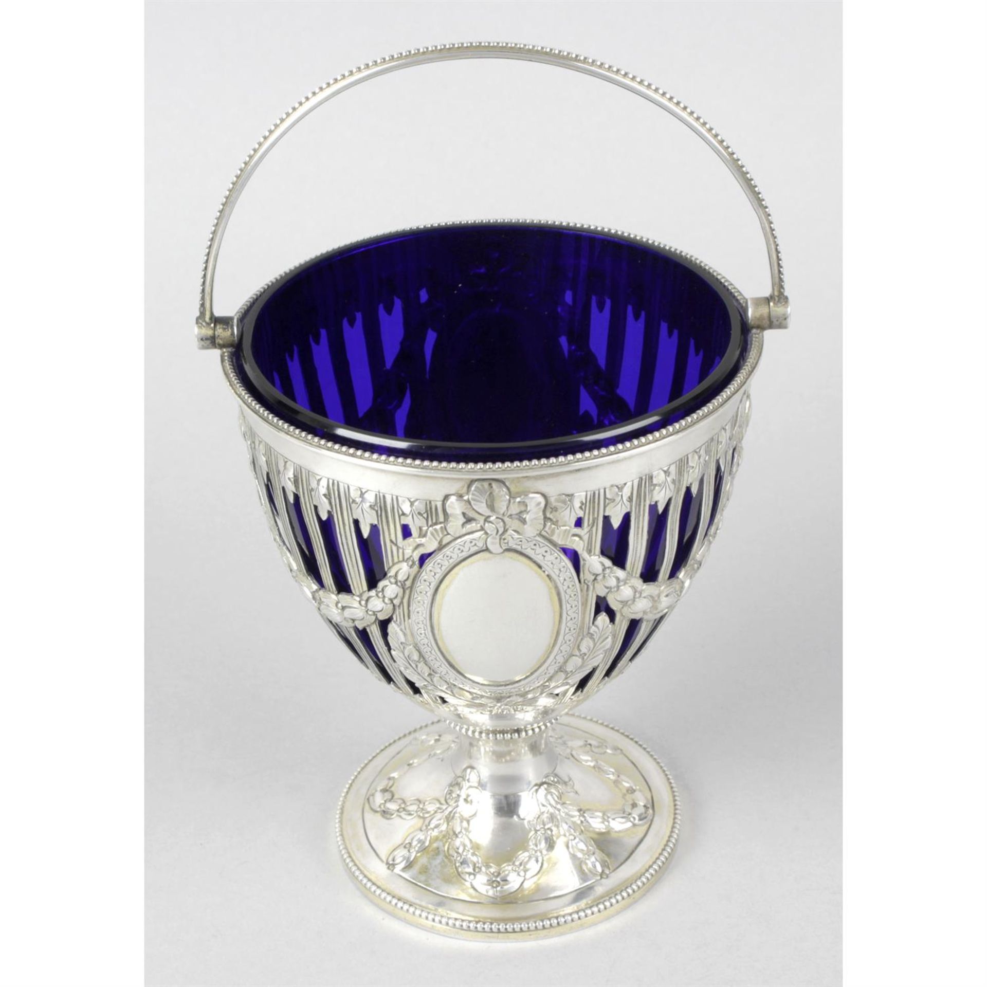 A Victorian silver pierced and swing-handled pedestal sugar basket with blue glass liner.