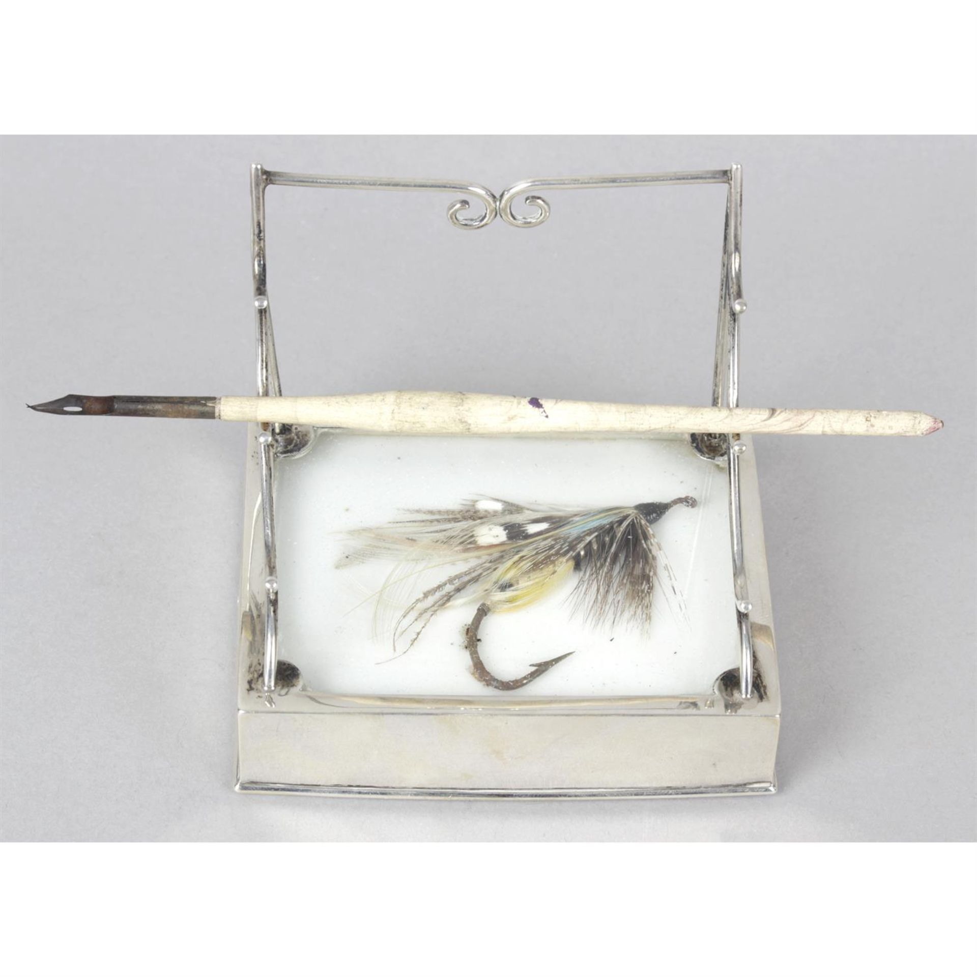 A silver combined pen stand and paperweight detailed with a fishing fly.