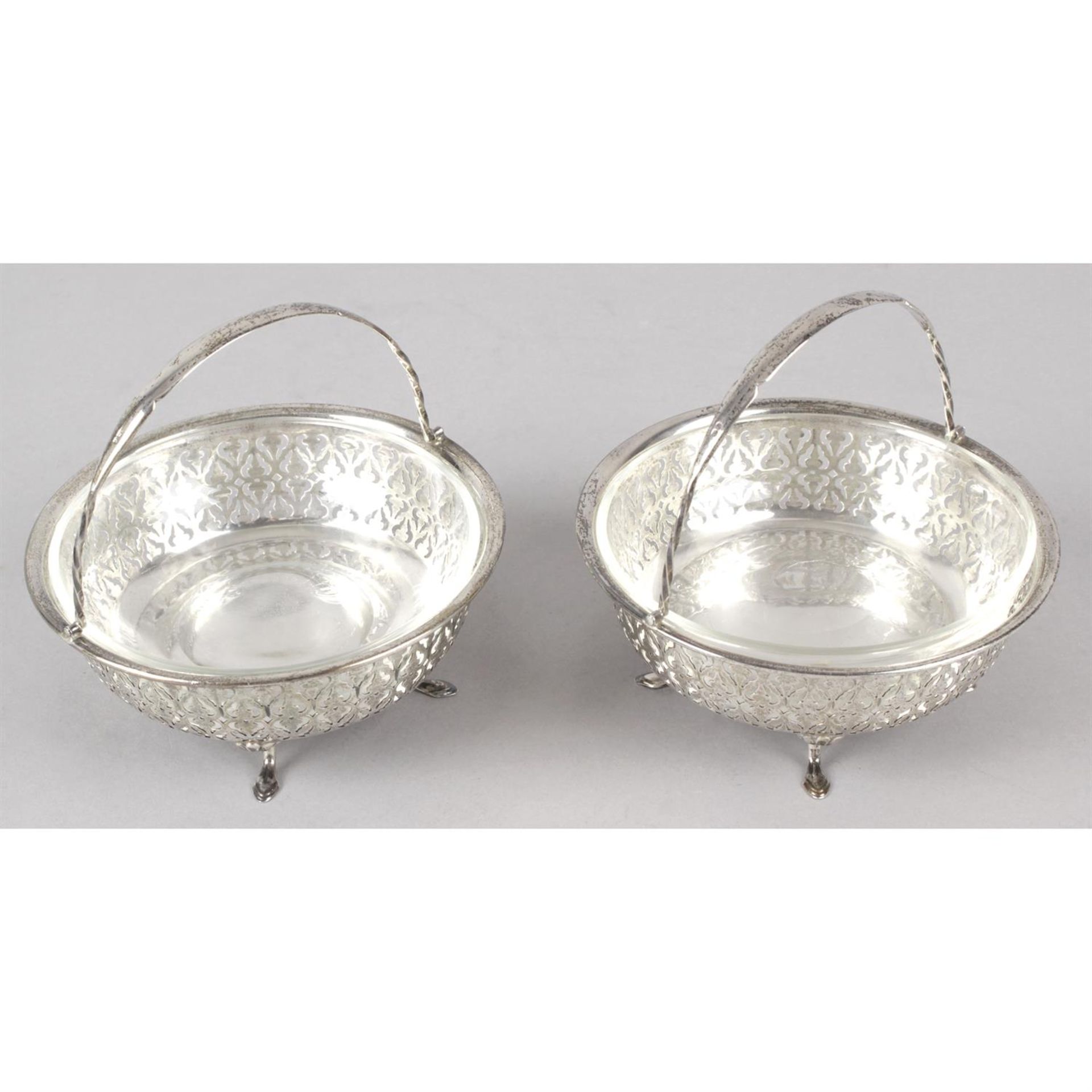 A pair of George V silver pierced swing-handle dishes with glass liners.