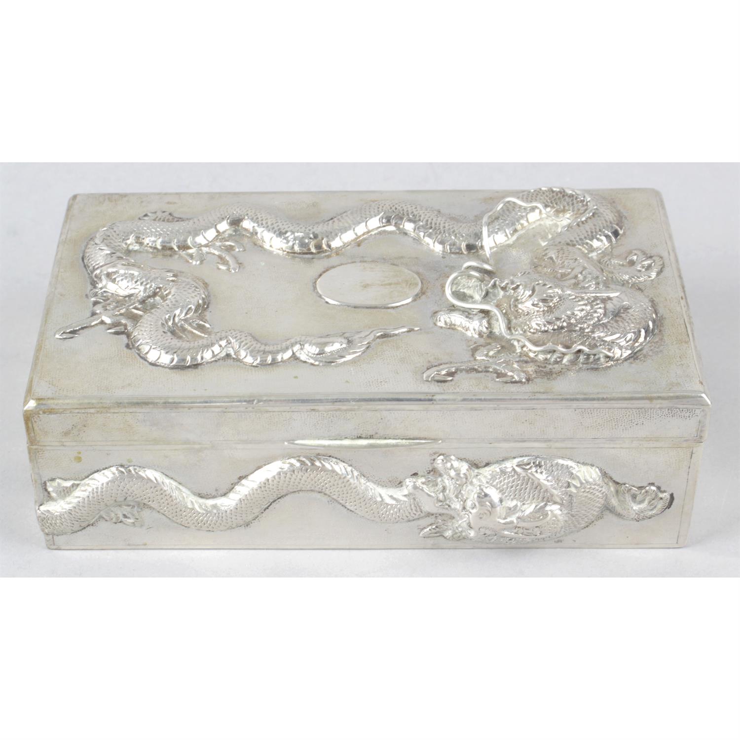 A Chinese export silver table cigarette box decorated with dragons in relief.