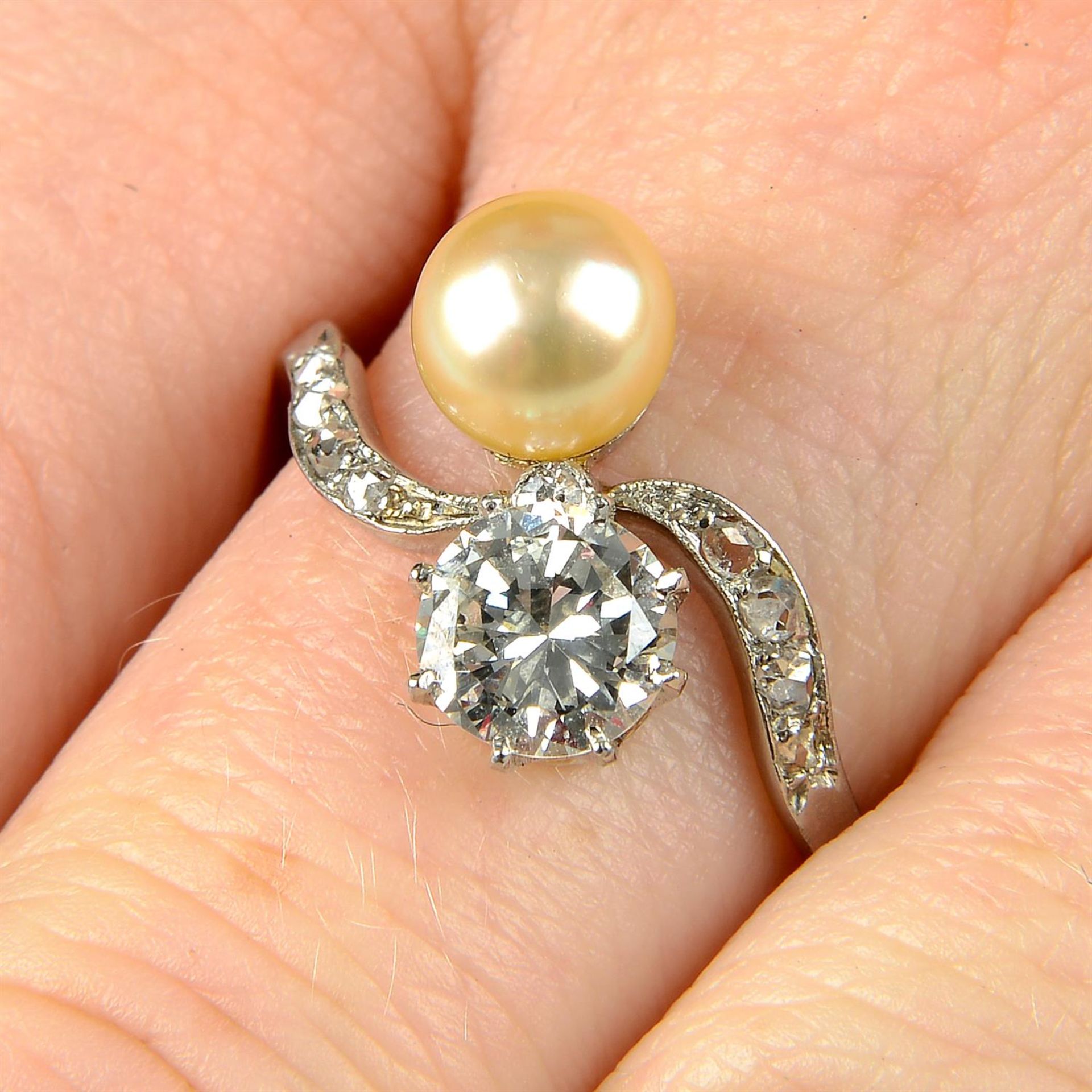 An early 20th century platinum, circular-cut diamond and pearl crossover ring.