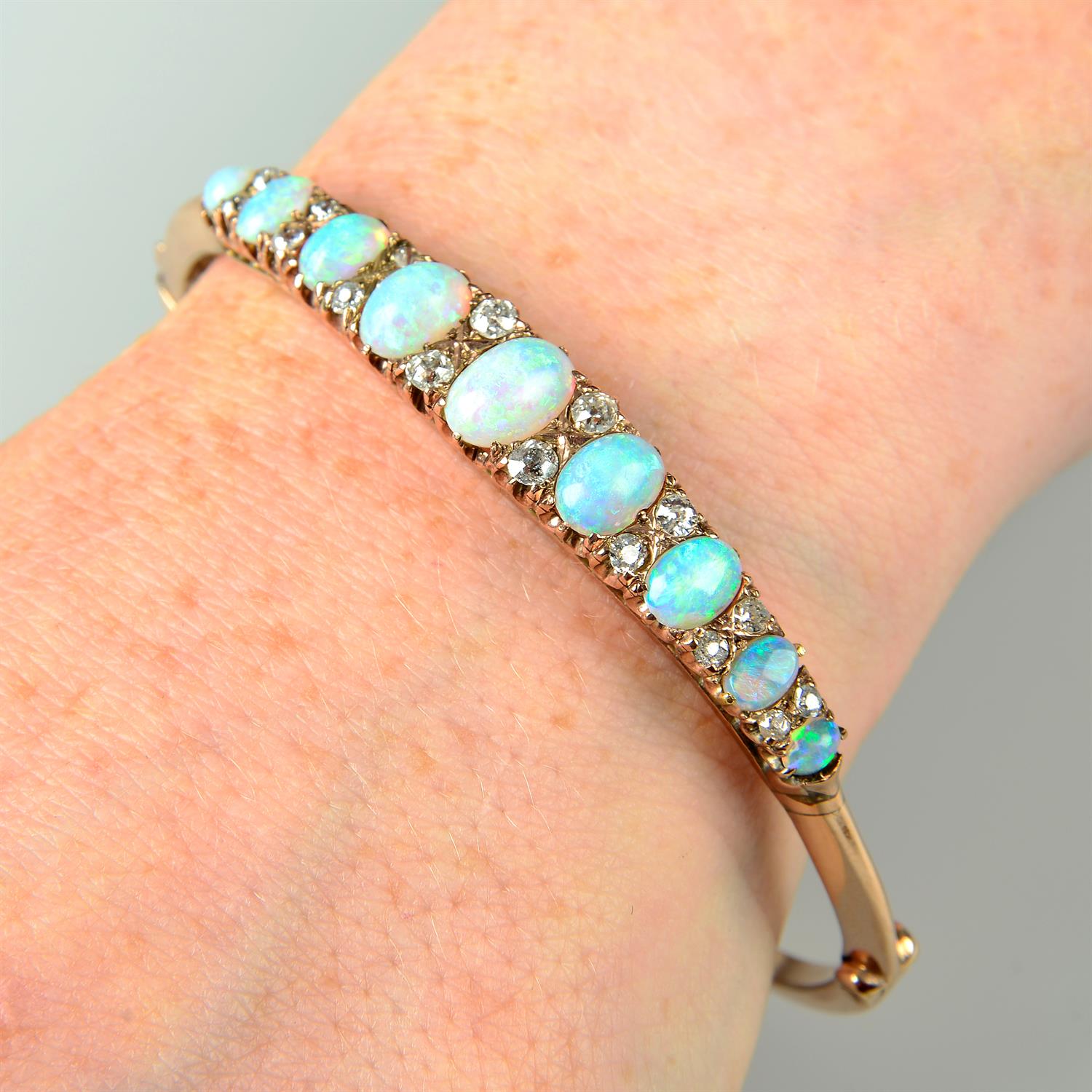 A late Victorian 9ct gold graduated opal hinged bangle, with old-cut diamond spacers.