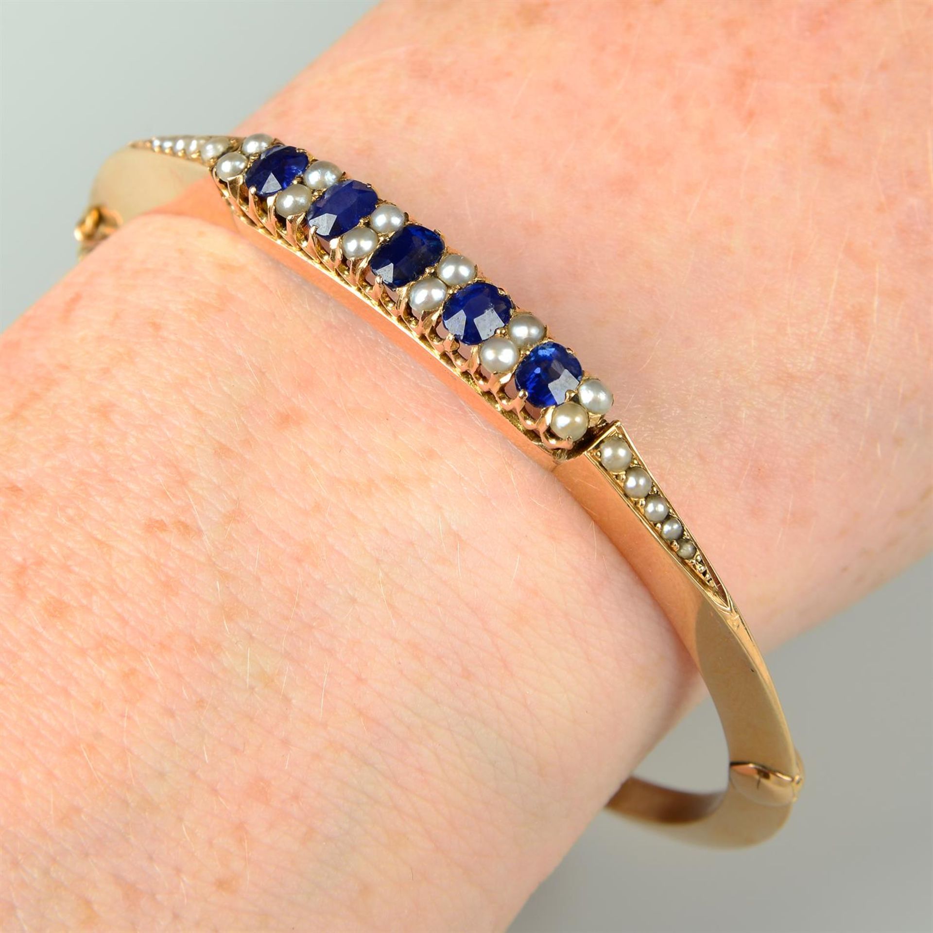 An early 20th century 18ct gold sapphire and split pearl hinged bangle.