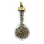 A pendant, designed to depict a glass flask, with yellow metal scraps.
