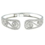 A brilliant-cut diamond hinged bangle with scrolling design.