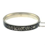 A late 19th century silver seed pearl and black enamel floral motif mourning bangle.