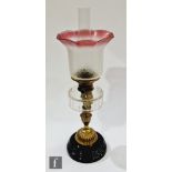 A Victorian brass oil lamp with part acid etched cranberry shade on a black glazed base, height
