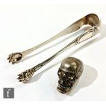 A plated skull vesta case with hinged jaw and a pair of French silver sugar tongs with claw bowls by