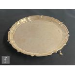 A hallmarked silver circular salver raised on three pad feet and terminating in pie crust border,