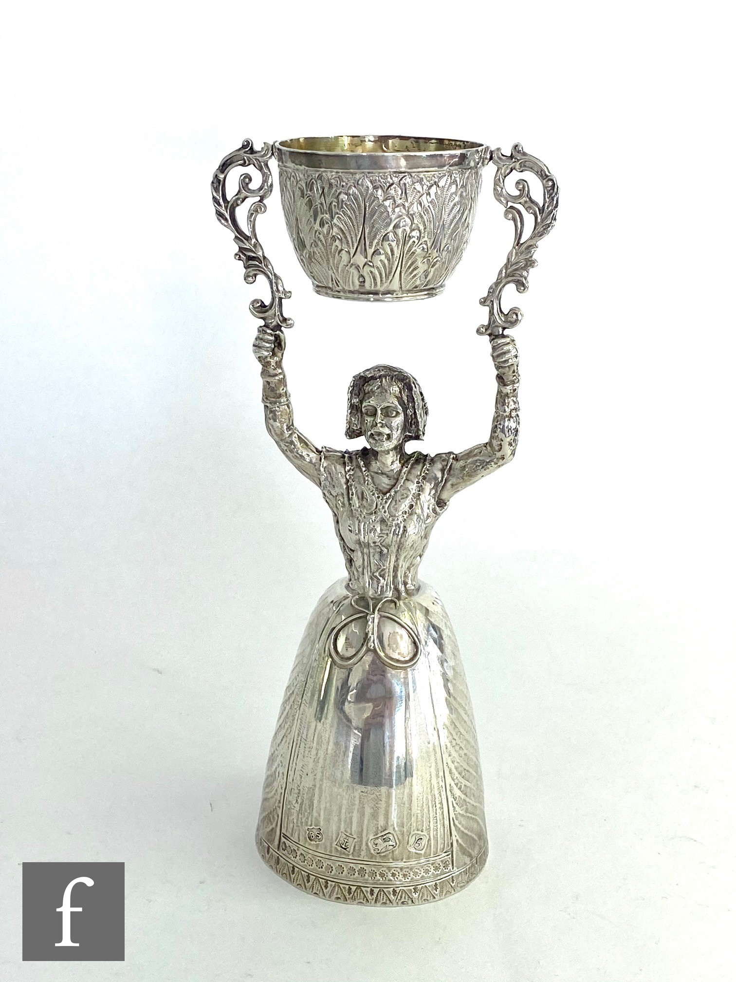 A modern hallmarked silver wager cup modelled as a women with arms raised supporting a small bowl,