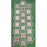 An early 20th Century patchwork blanket decorated with honeycomb patterns against a pea green