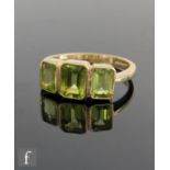 A 9ct hallmarked three stone peridot ring, emerald cut collar set stones to knife edged shoulders,