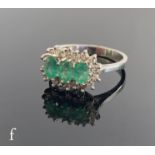 An 18ct white gold emerald and diamond cluster ring, three central claw set oval emeralds within a