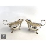 A pair of hallmarked silver sauce boats each with waved borders, flying scroll handles and raised on