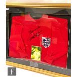 A framed England red football shirt signed 'Best wishes Geoff Hurst', inset with photograph of Geoff