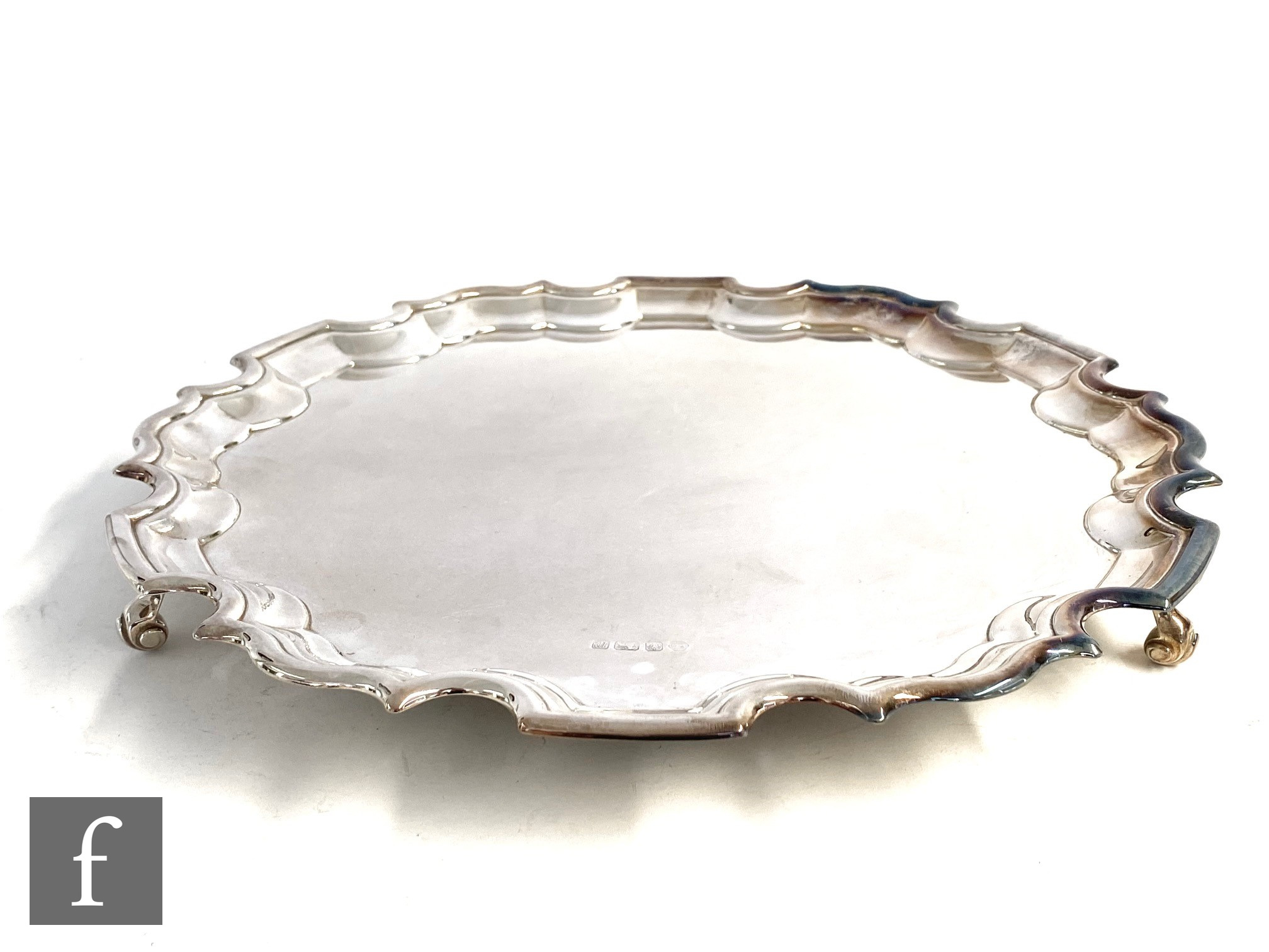 A hallmarked silver circular salver of plain form terminating in scalloped border and raised on