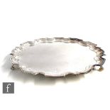 A hallmarked silver circular salver of plain form terminating in scalloped border and raised on