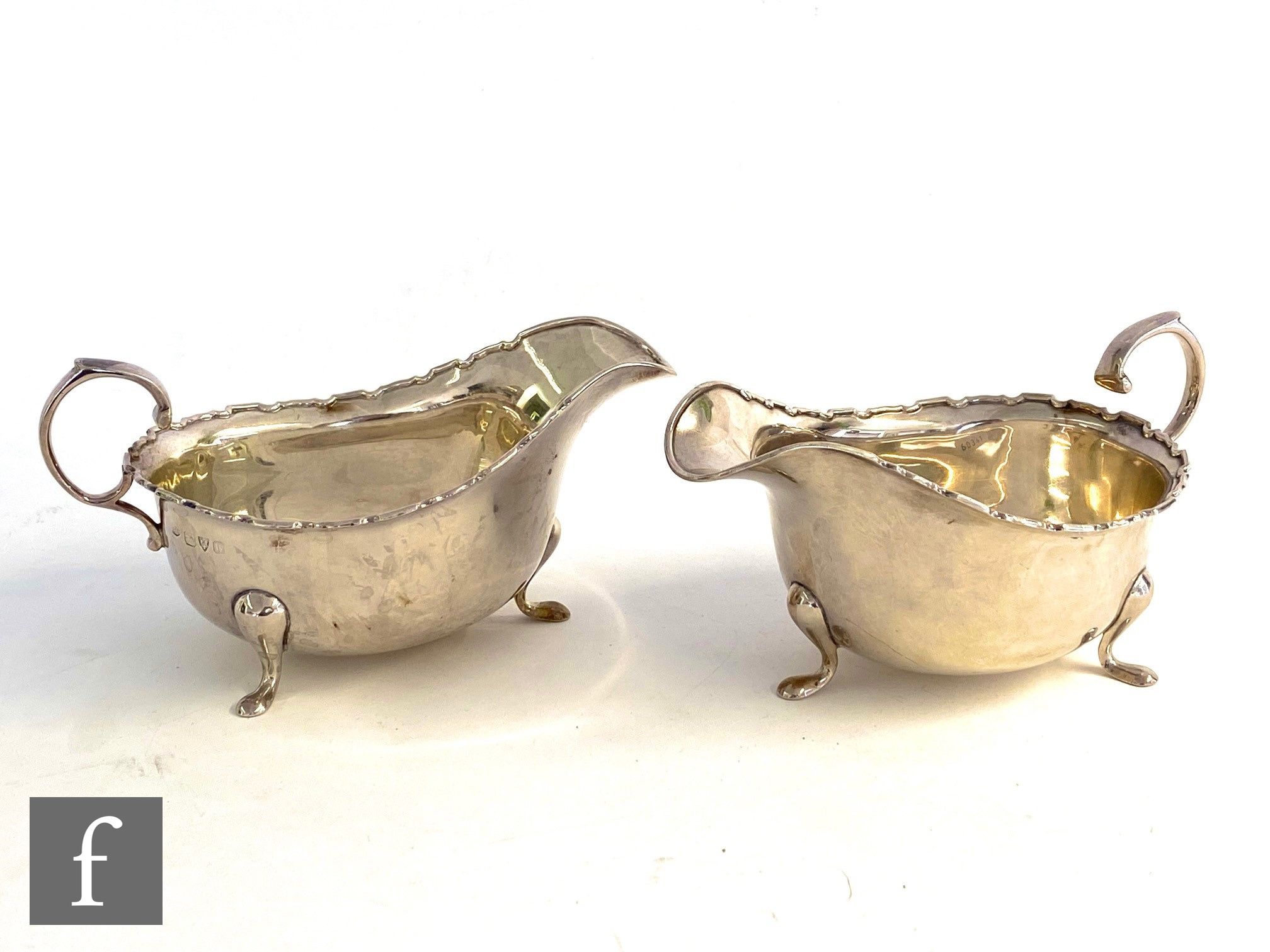 A pair of hallmarked silver sauce boats each raised on three pad feet and terminating in scalloped