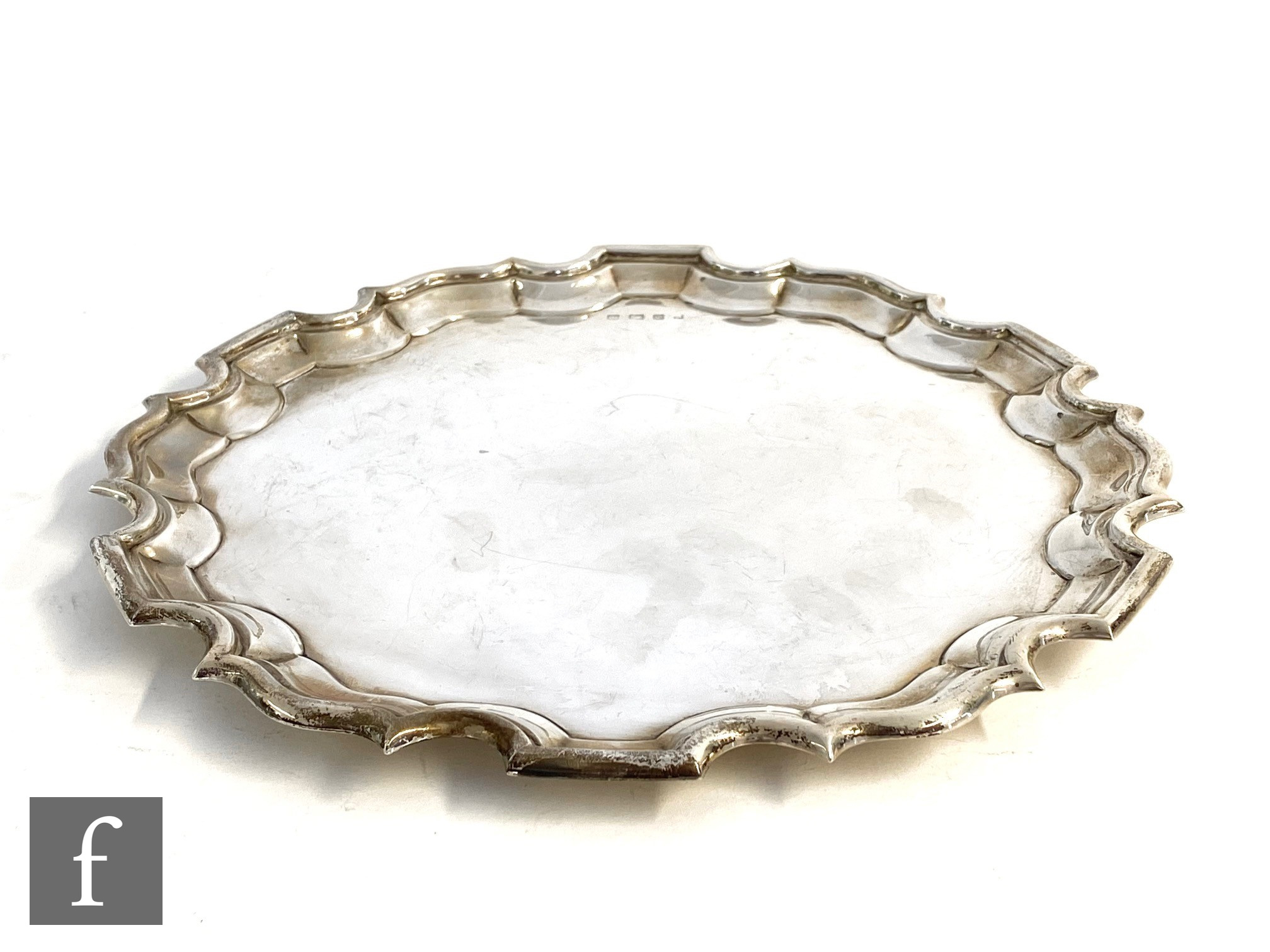 A hallmarked silver circular salver of plain from terminating in pie crust border, raised on three