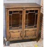 An early 20th Century oak double door display cabinet, with lunette frieze above the bar glazed