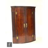 A George III oak bow front hanging corner cupboard enclosed by a pair of doors flanked by reeded