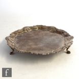 A George II hallmarked silver card waiter of plain form with shell detailed border and raised on