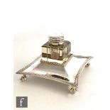 A silver plated and clear glass ink well and stand, shaped square plated stand with gadroon