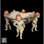 A Dresden table centre fruit basket modelled as four standing cherubs supporting a shaped bowl on