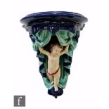 A 19th Century Wedgwood majolica wall bracket modelled as a cherub holding a swagged curtain open,