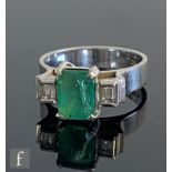 An Art Deco 18ct emerald and diamond three stone ring, central claw set emerald cut emerald,