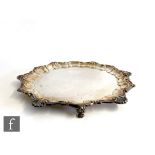 A hallmarked silver circular salver of plain form with scallop and shell border, raised on three